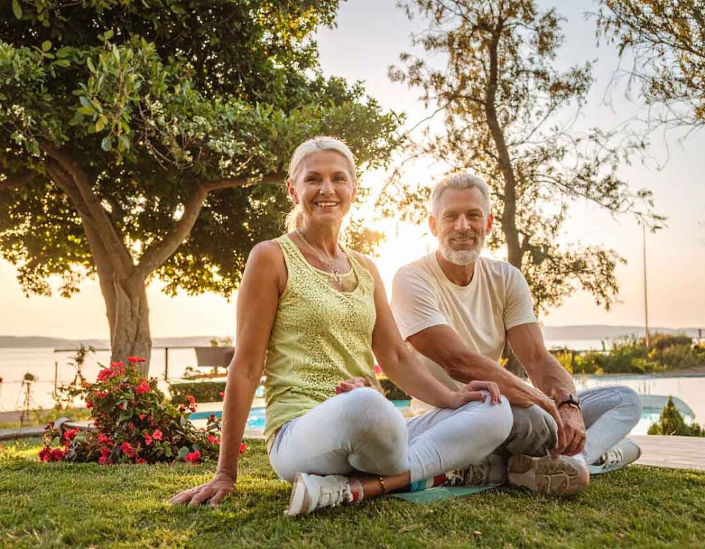 Sportlich gekleidetes Rentnerehepaar in den 50ern sitzt entspannt im gemütlichen Garten mit Blick auf den Balaton – idealer Alterswohnsitz am Plattensee in Ungarn.