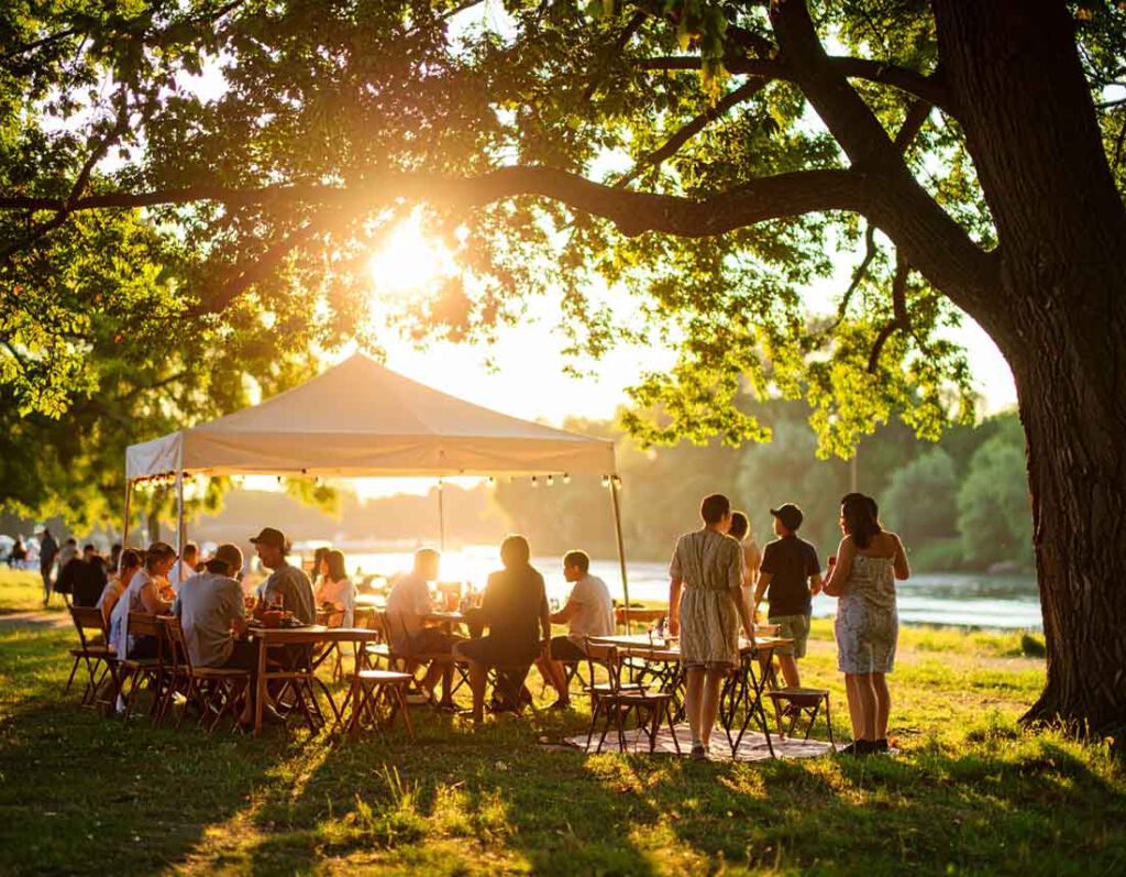 Menschen beim sommerlichen Picknick unter einem Pavillon am Fluss in Békéscsaba, Südostungarn – Sonnenlicht fällt durch die Bäume und schafft eine friedliche Atmosphäre im Grünen