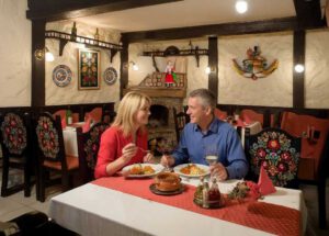 Ein Paar genießt ungarische Spezialitäten in einem traditionell eingerichteten Restaurant mit folkloristischer Dekoration und gemütlicher Atmosphäre. Abendessen wie in Szentloerinc